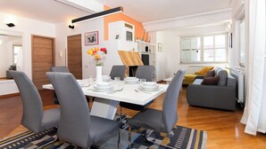 Una sala de estar moderna con comedor, con una mesa blanca, sillas grises y un sofá con cojines.