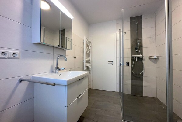 A modern bathroom with a white sink, mirror, and glass shower enclosure.