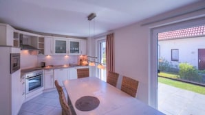 Une cuisine moderne avec des meubles blancs, une table à manger avec des chaises et une vue sur un jardin grâce à de grandes fenêtres.