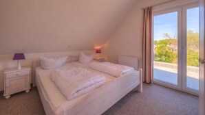 Une chambre avec un grand lit, une table de chevet, une lampe et une vue sur l’extérieur, accessible par une porte-fenêtre coulissante.