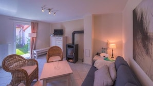 Un salon chaleureux avec un canapé, une table, des fauteuils en osier, une cheminée et une vue sur l’extérieur.