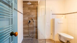 A modern bathroom with a glass shower enclosure, a wooden wall, a white toilet, and a glass door with a round handle. - Ferienhaus mit großer Terrasse (Rechlin)