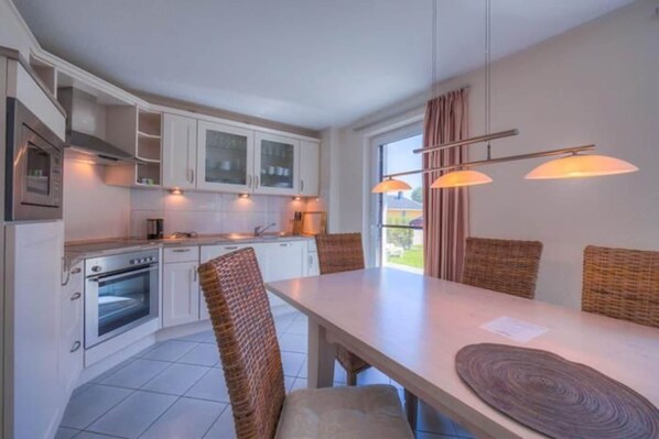 A modern kitchen with white cabinets, a built-in oven, and a dining area with wicker chairs and a table.