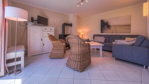 A modern living room with a sofa, two wicker chairs, a coffee table, a TV on a cabinet, and a painting on the wall. - Ferienhaus mit großer Terrasse (Rechlin)