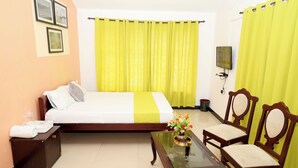 A hotel room with a bed, a small table with a vase of flowers, two wooden chairs, a nightstand, and a television on the wall. - ELK HILL PALACE (Ootacamund)
