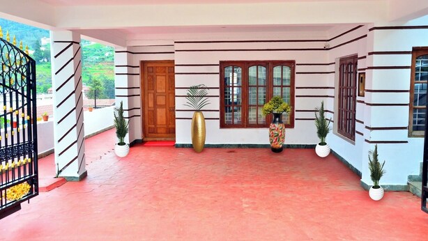 A covered entrance area with a red floor, a wooden door, and potted plants. - ELK HILL PALACE (Ootacamund)