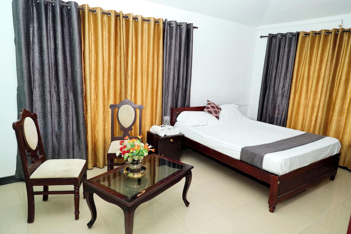 A hotel room with a bed, a chair, a small table with a vase of flowers, and curtains.