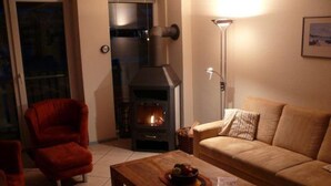 Un salon chaleureux avec une cheminée, un fauteuil rouge, un canapé beige et une table basse en bois.