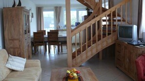 Un salon avec un escalier en bois, un coin repas et un téléviseur posé sur un meuble en bois.