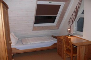 A small, cozy room with a sloped ceiling, a single bed, a wooden desk, and a window.