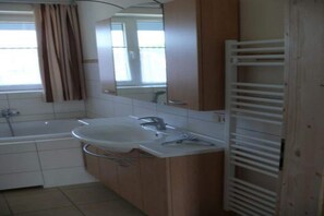 A bathroom with a bathtub, a sink, a mirror, and a window with curtains.