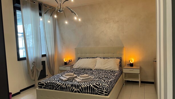Een moderne slaapkamer met een groot bed, twee nachtkastjes met lampen, een plafondlamp en dunne gordijnen.