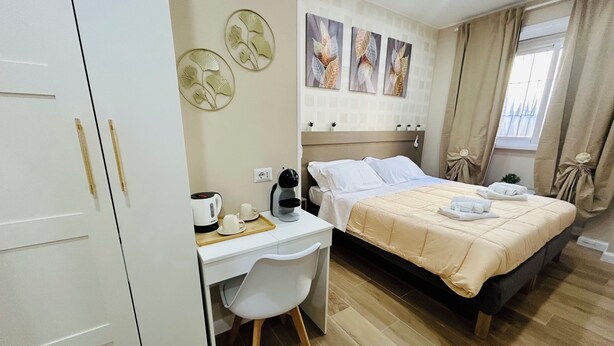 A hotel room with a bed, a desk with a chair, a coffee maker, and wall art. - Segesta Rooms  (Rome)