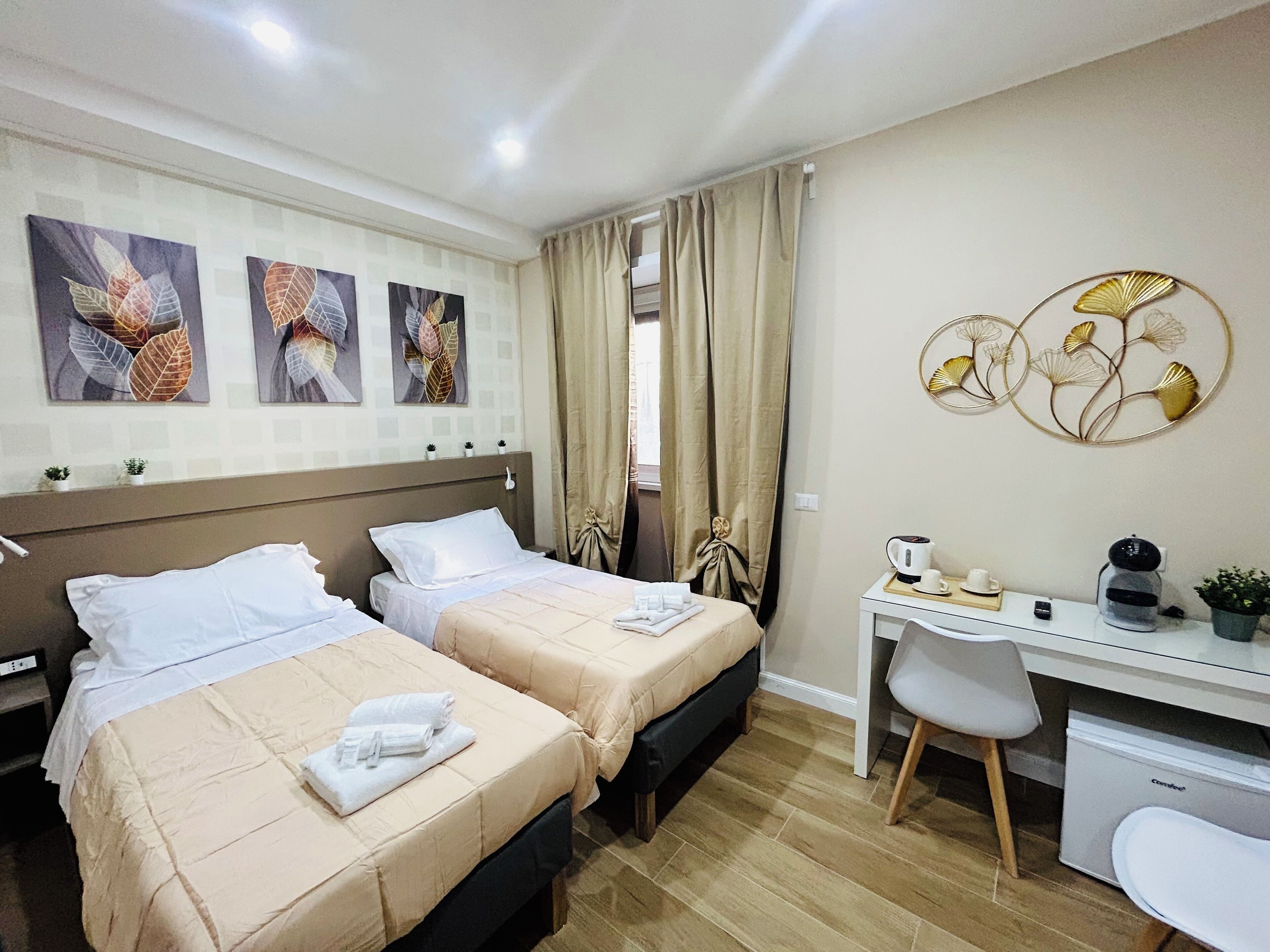 Une chambre d’hôtel avec deux lits, un bureau et une chaise. On y trouve des œuvres d’art décoratives accrochées au mur, ainsi qu’une petite plante posée sur le bureau.