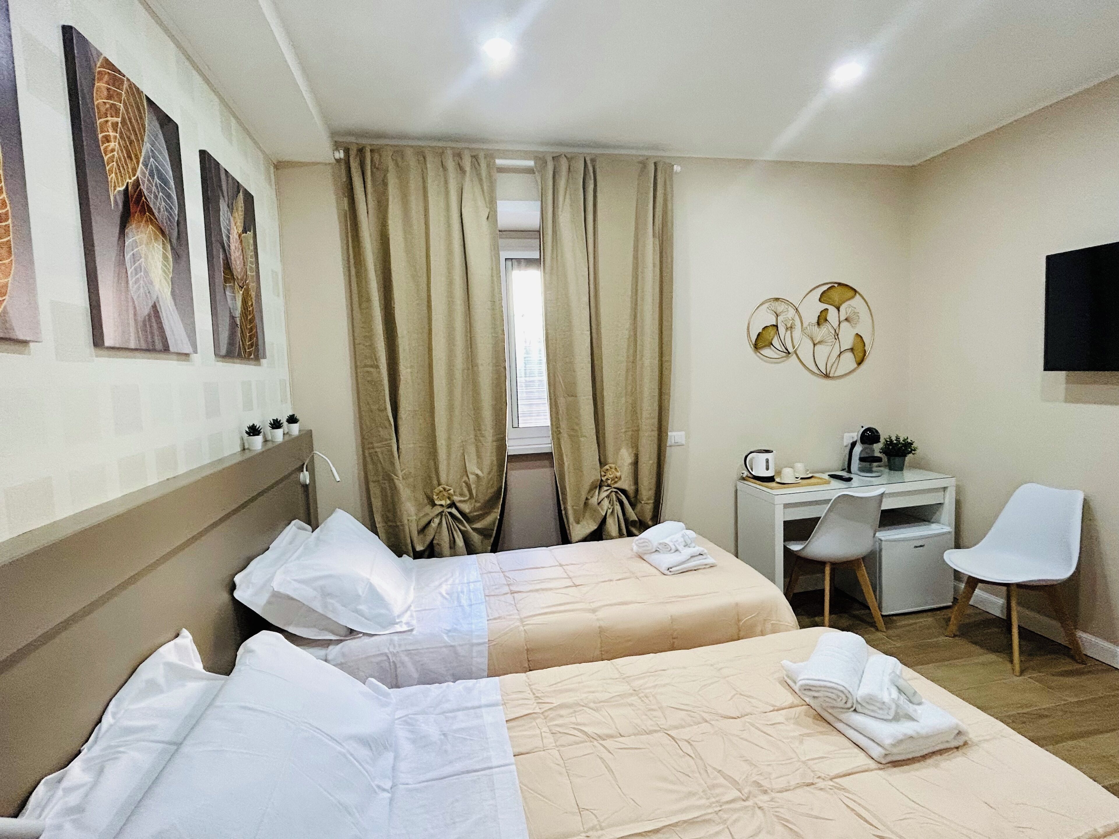 A hotel room with two beds, a desk, a chair, a TV, and artwork on the wall.
