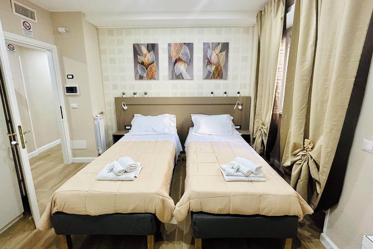 A twin room with two beds, a radiator, a door, and three wall-mounted artworks.