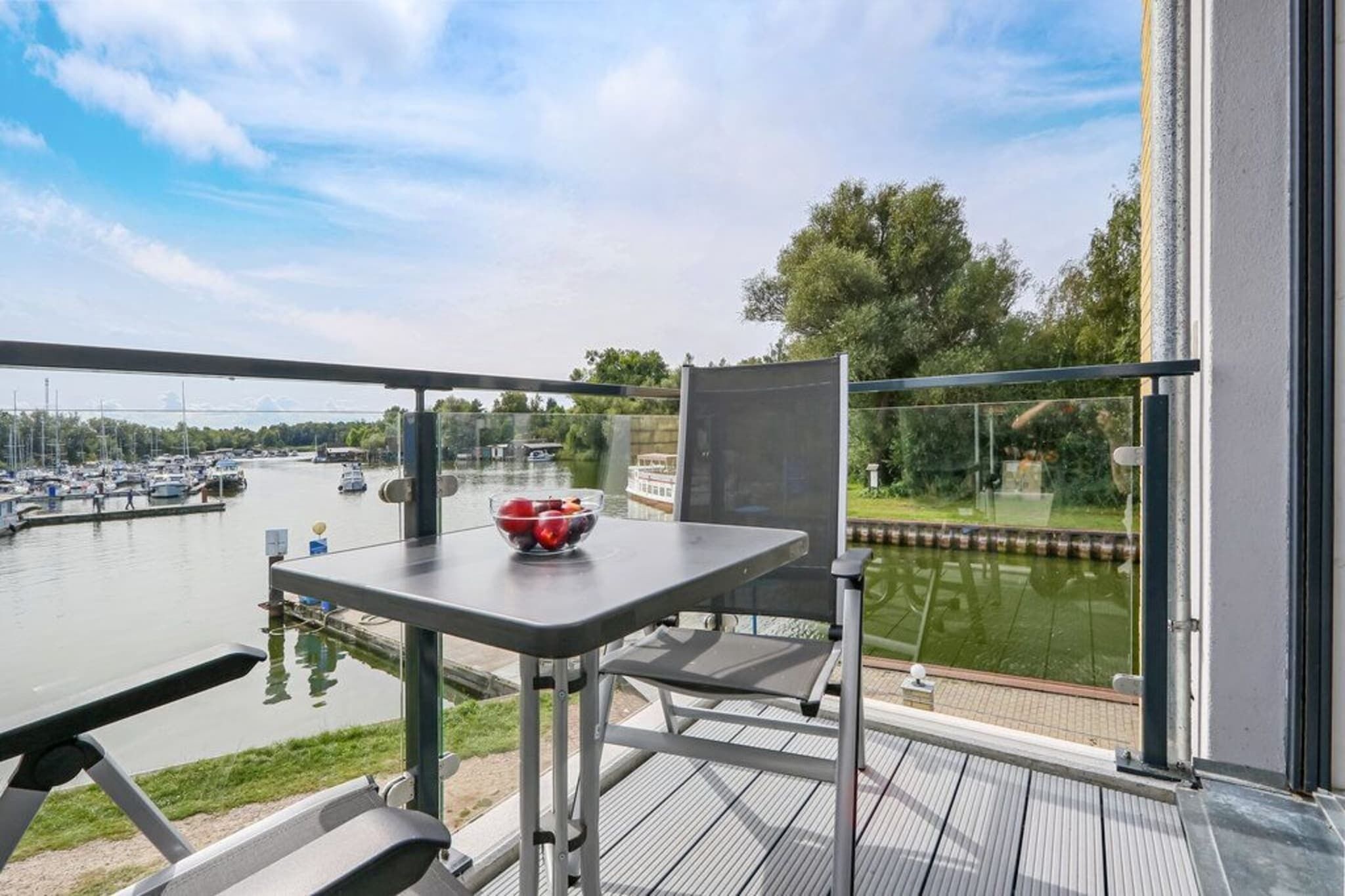 En balkon med et bord og en stol, der giver udsigt over en lysthavn med både.