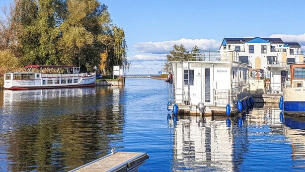Une rive bordée d’une péniche amarrée au quai, entourée d’arbres et sous un ciel dégagé.