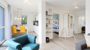 Un salon moderne avec un canapé bleu, un coin repas avec des chaises jaunes et une cuisine en arrière-plan.