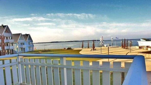 En vacker utsikt över kusten från en balkong med ett vitt räcke, med utsikt över en strand och en rad hus.
