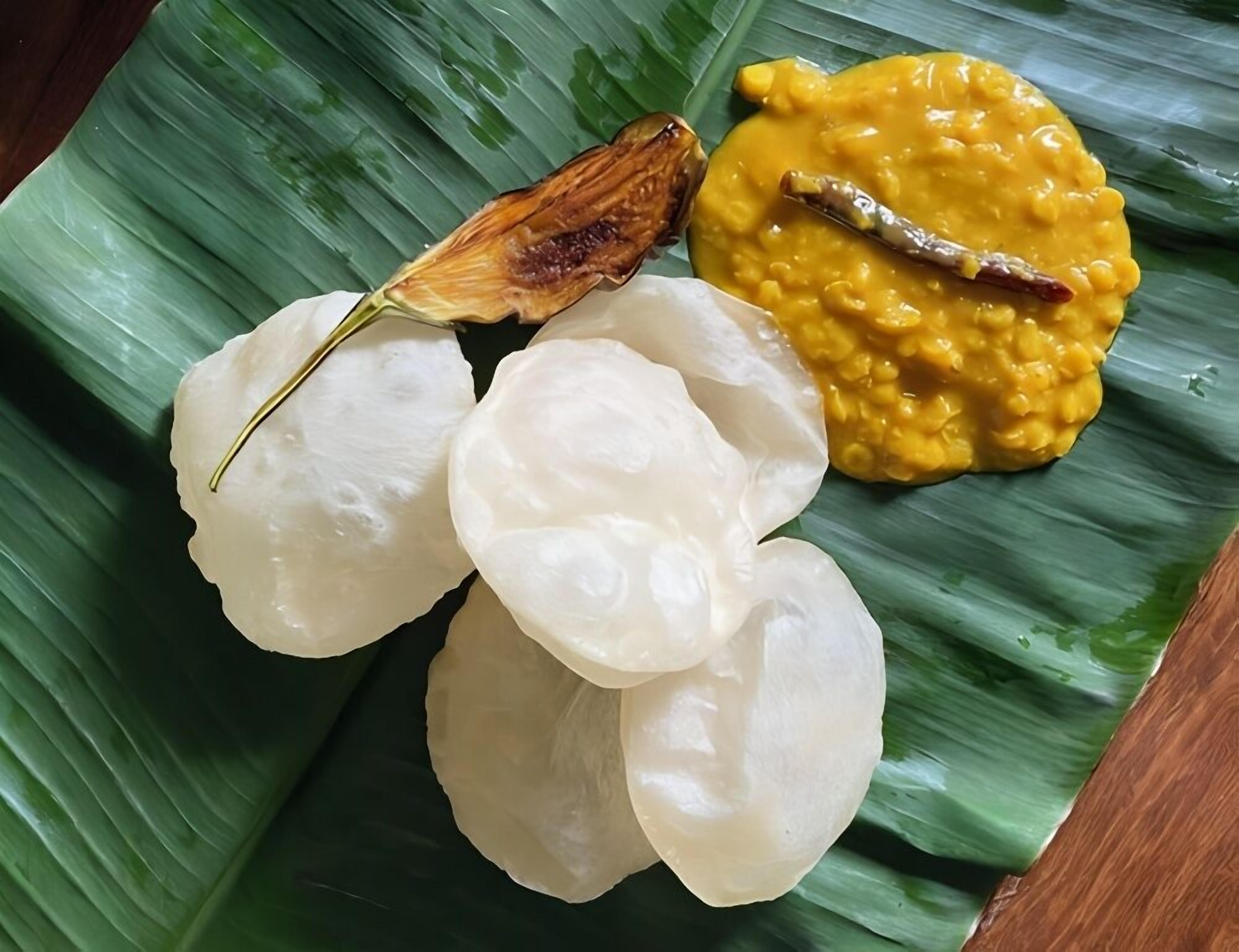 A plate of food with white rice cakes, a yellow curry, and a fried item on a banana leaf.