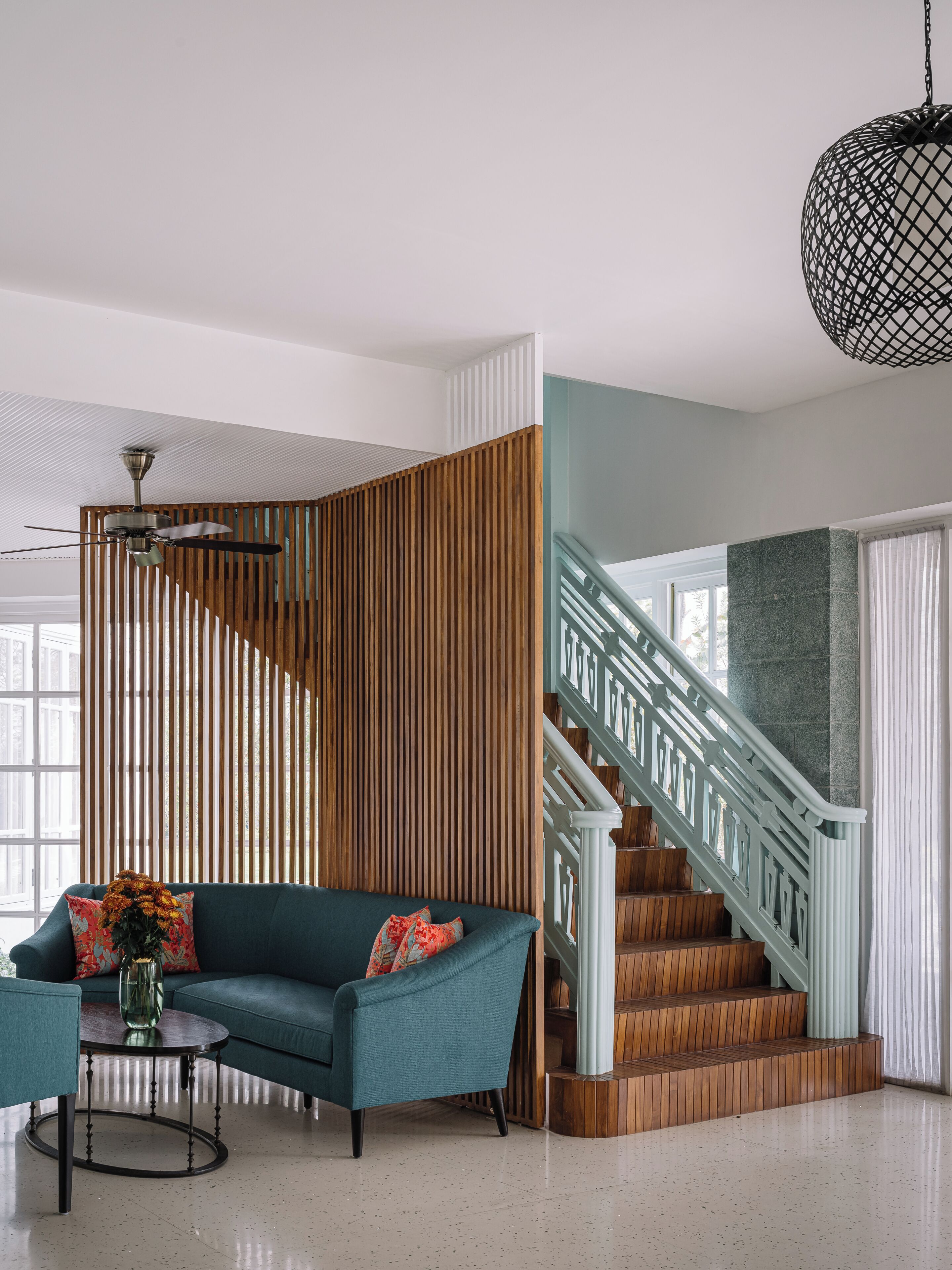 Een modern interieur met een smaragdgroene bank, een houten lattenwand, een trap met witte leuningen en een hanglamp.