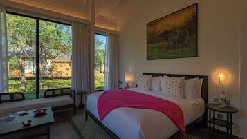 A hotel room with a large bed, a bench, a dining table, and a view of the outdoors.