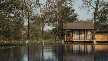 A wooden cabin with a balcony, surrounded by trees and a body of water.