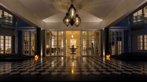 Un ingresso hotel con pavimento a scacchi, ampie porte in vetro e un lampadario.