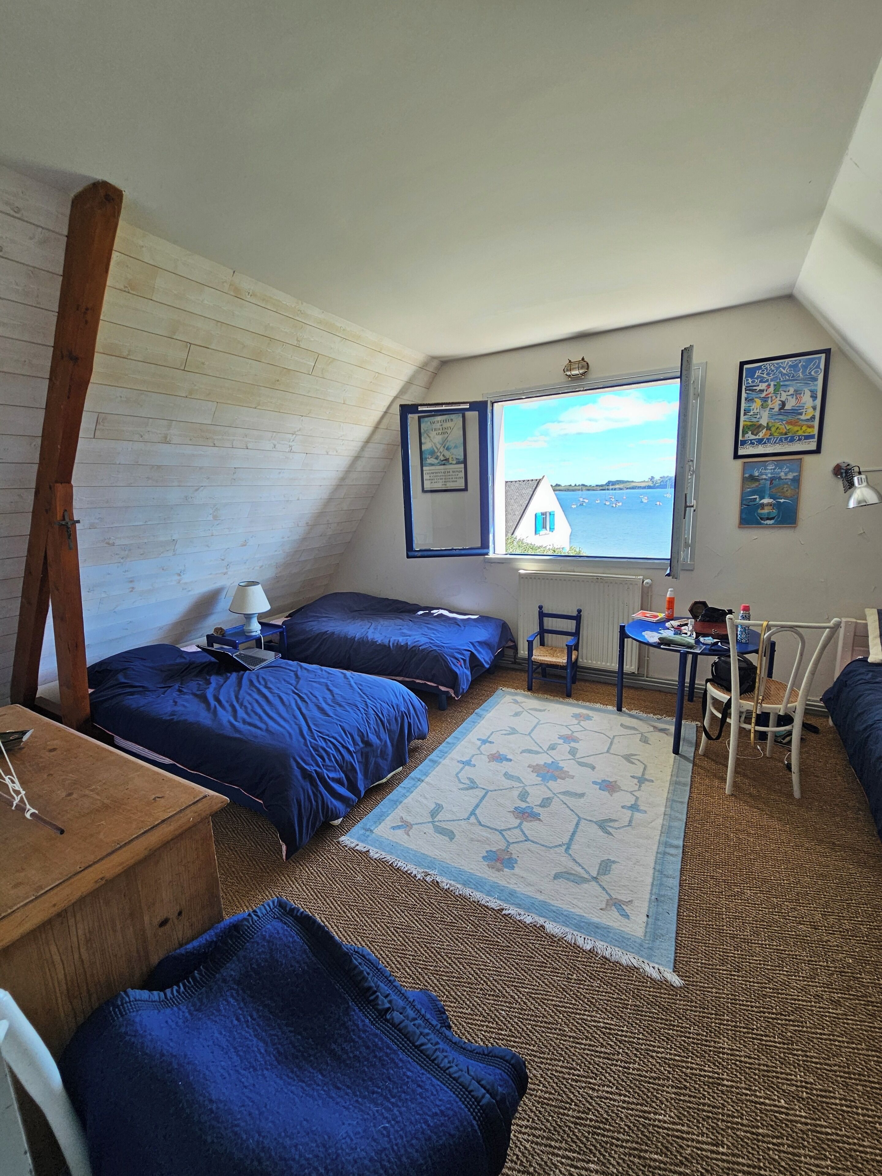 Una habitación acogedora con dos camas, un escritorio pequeño, una silla y una ventana con vista al mar.