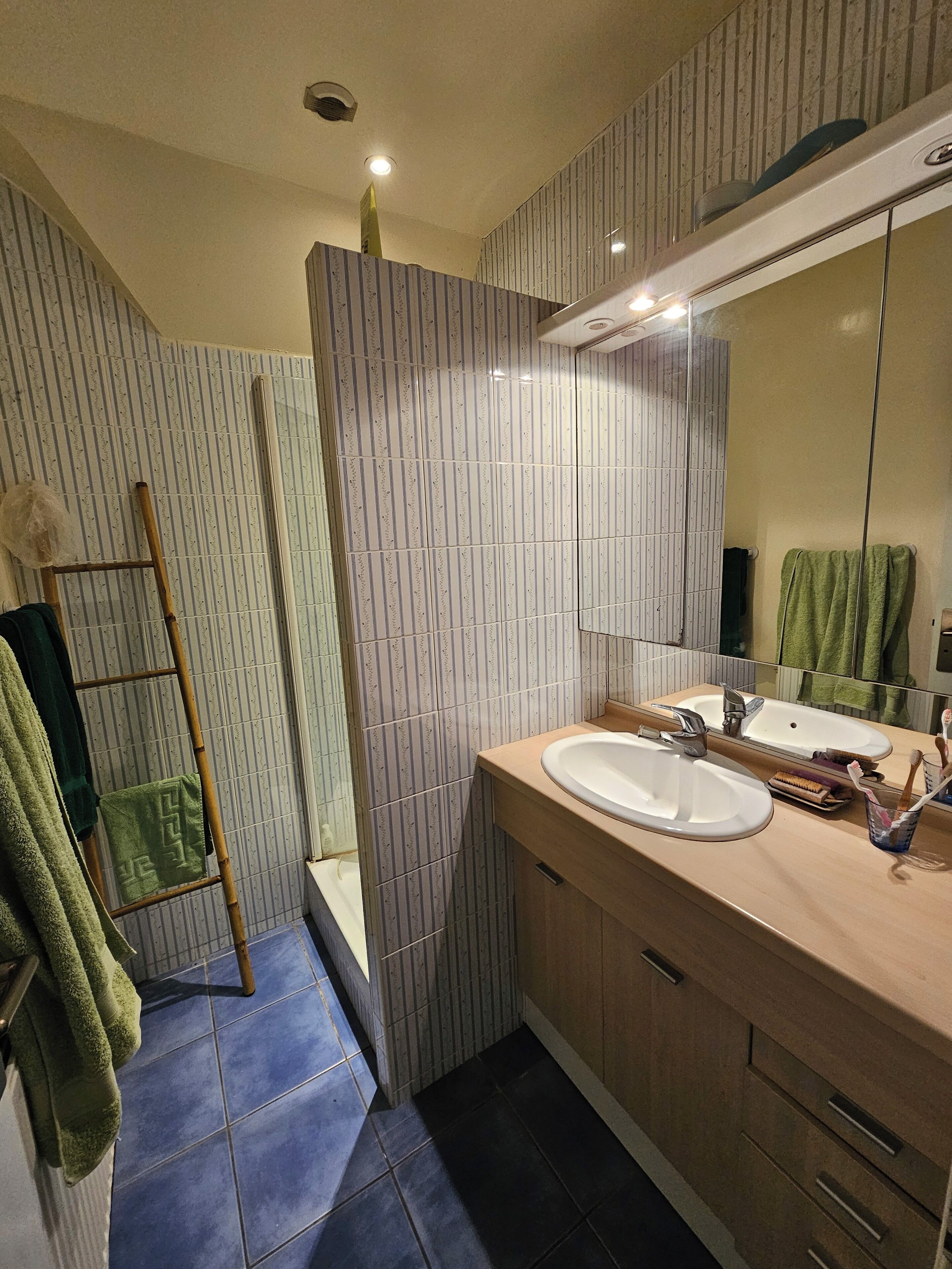 Een moderne badkamer met streepjestegels, een houten trap, een wastafel en een spiegel.