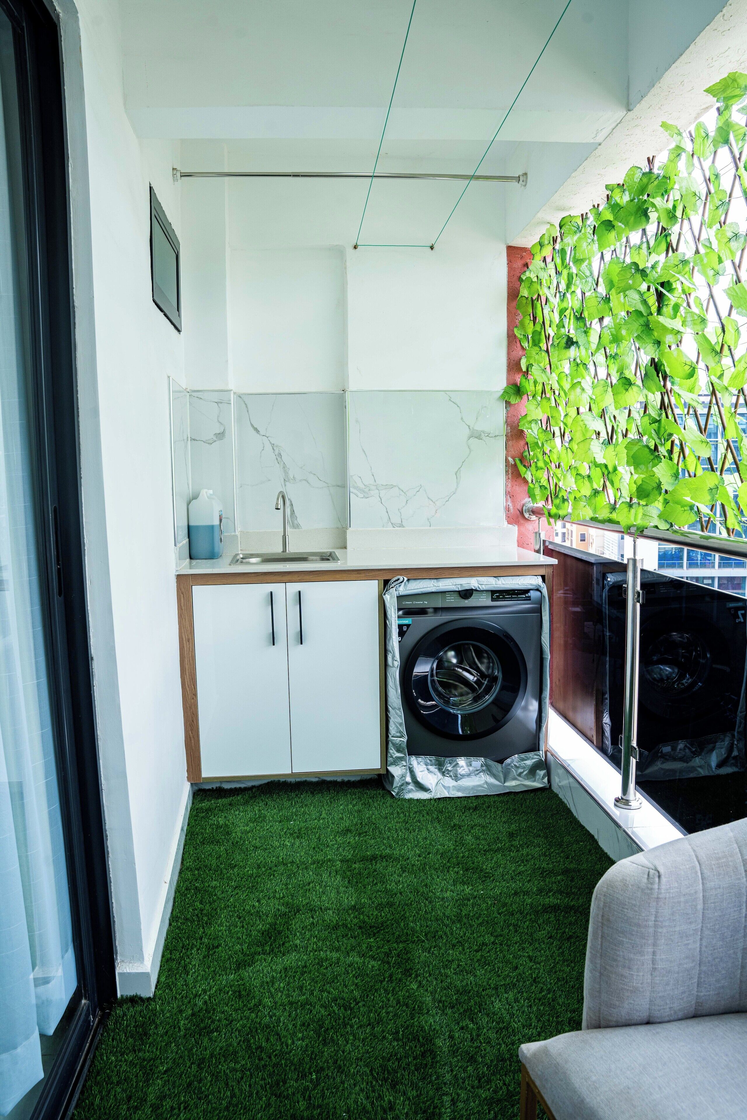 Una cocina compacta con armarios blancos, lavadora integrada y piso de césped artificial verde.