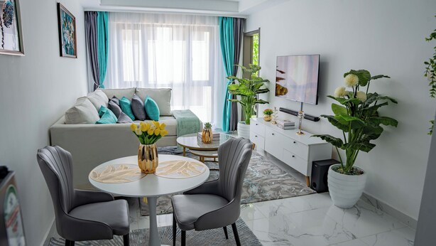 Een moderne woonkamer met een bank, twee grijze stoelen, een salontafel en een televisie.