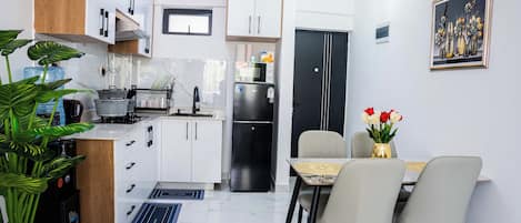Una cocina moderna con armarios blancos, un refrigerador negro y una zona de comedor con dos sillas y una mesa.