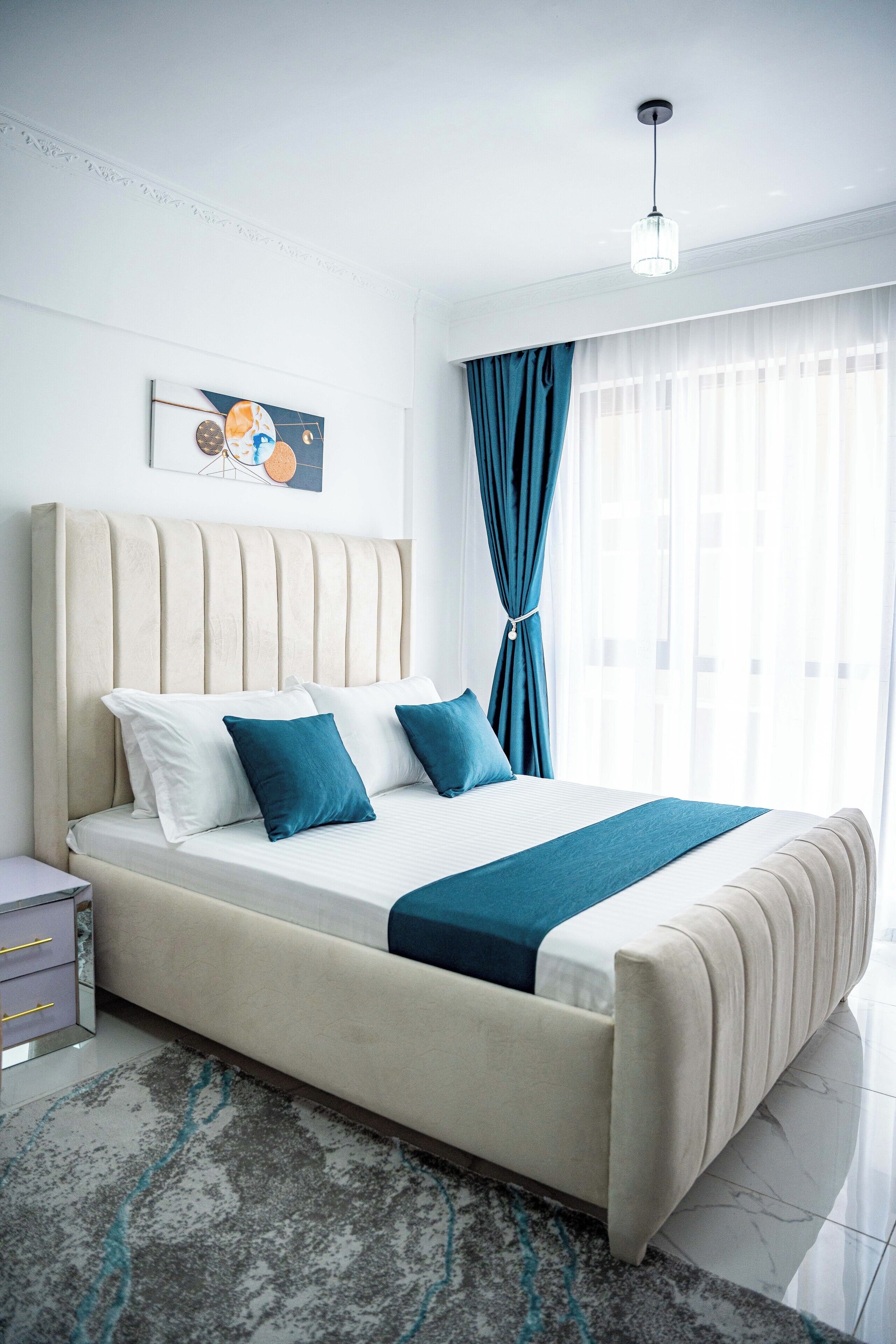 A modern bedroom with a large bed, a nightstand, a lamp, and a painting on the wall.