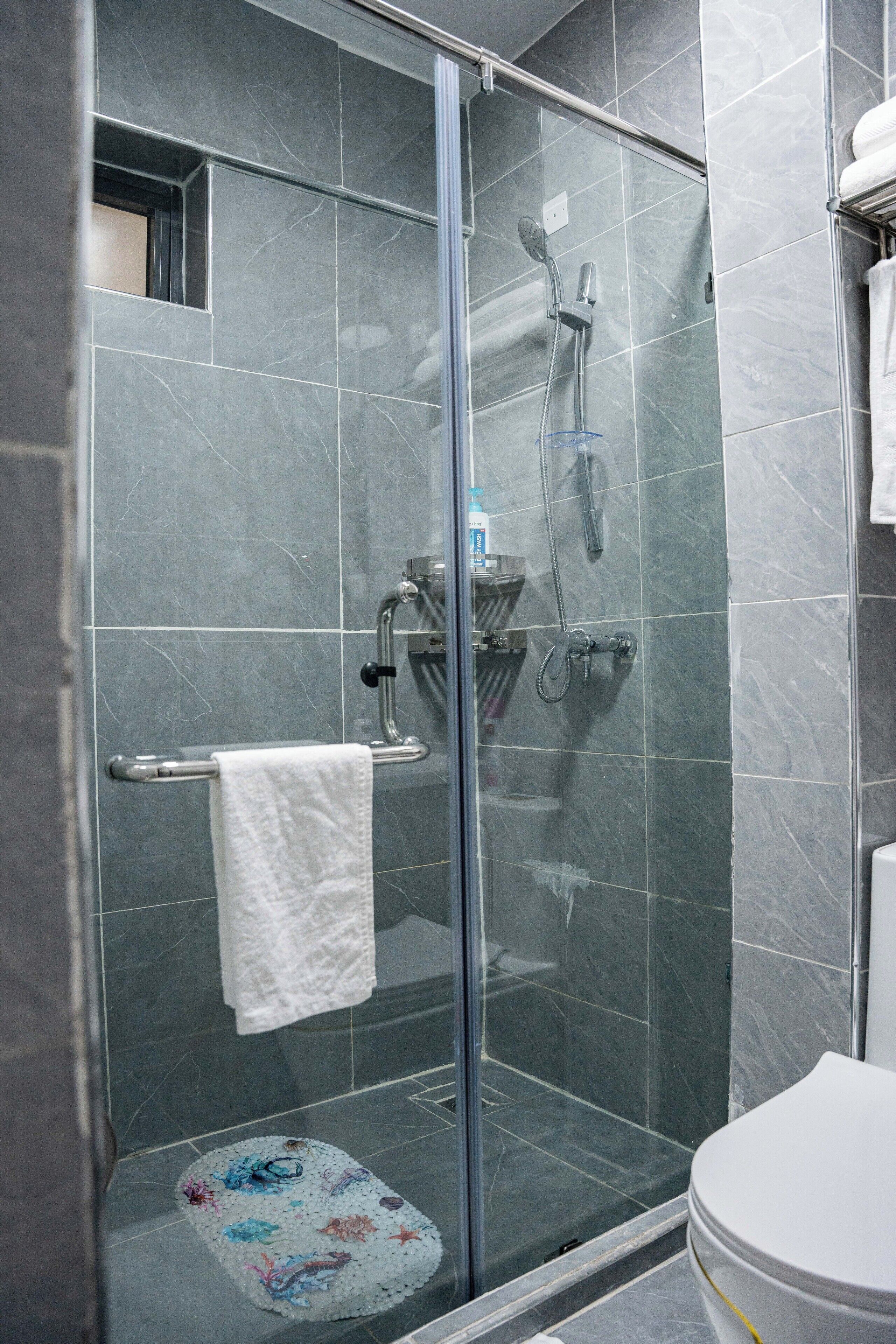 Une salle de bain moderne avec une douche à parois de verre, des toilettes blanches et une petite étagère contenant des articles de toilette.