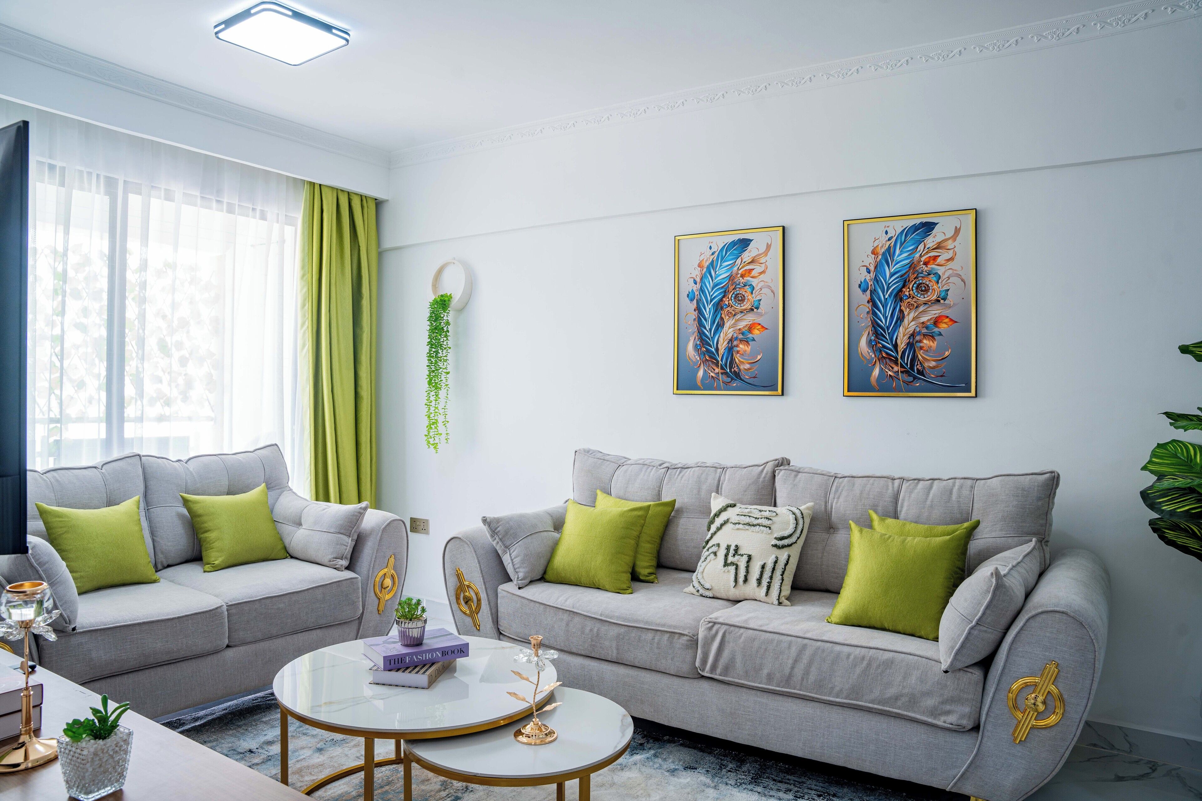 Una sala de estar moderna con dos sofás grises, cojines verdes, una mesa redonda de centro y dos obras de arte enmarcadas en la pared.