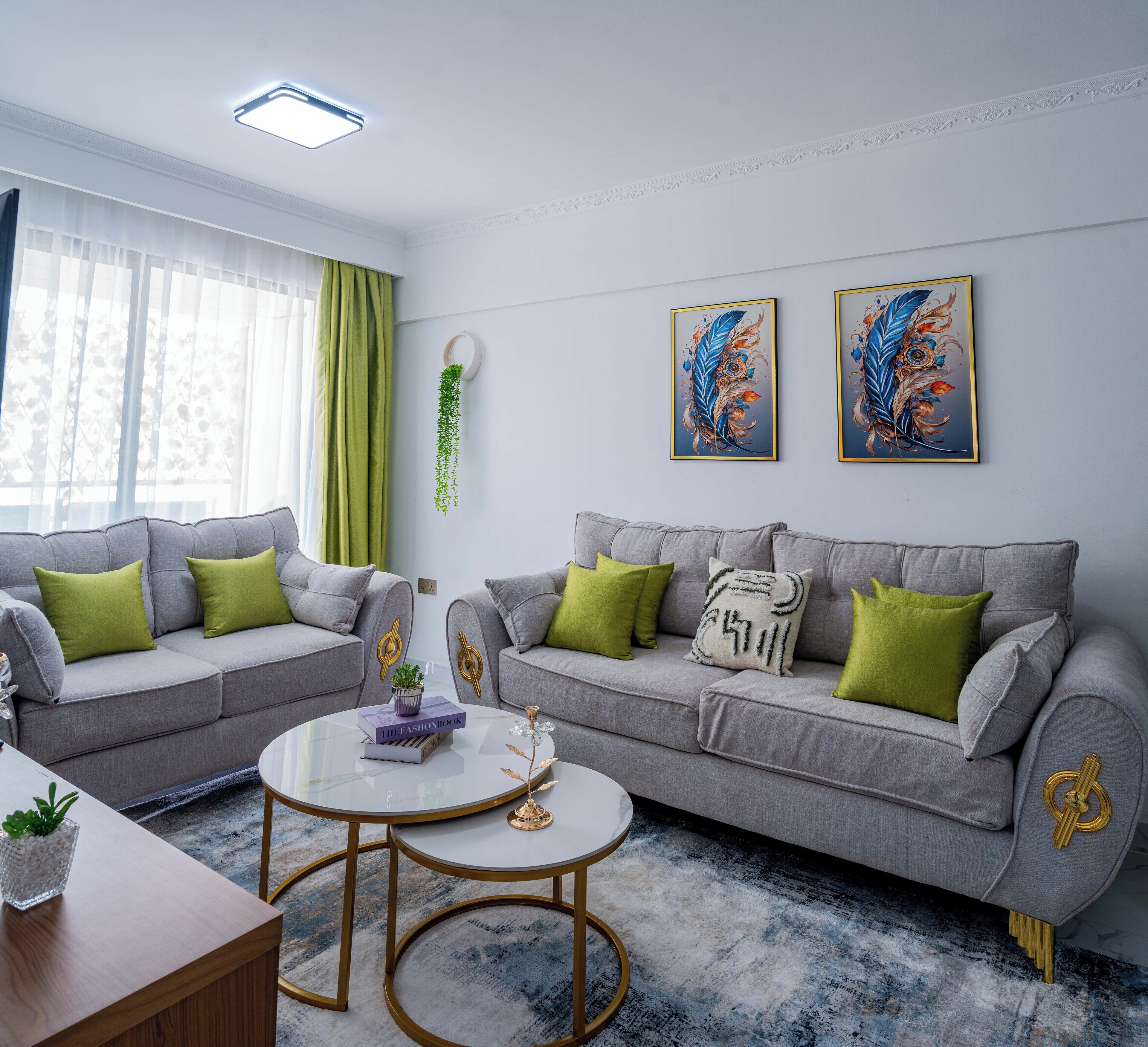Een moderne woonkamer met twee grijze banken, groene kussens, een glazen salontafel en decoratieve objecten.