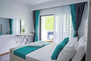 A hotel room with a bed, a mirror, a window with curtains, and a view of greenery outside. - Maskan Suites (Nairobi)