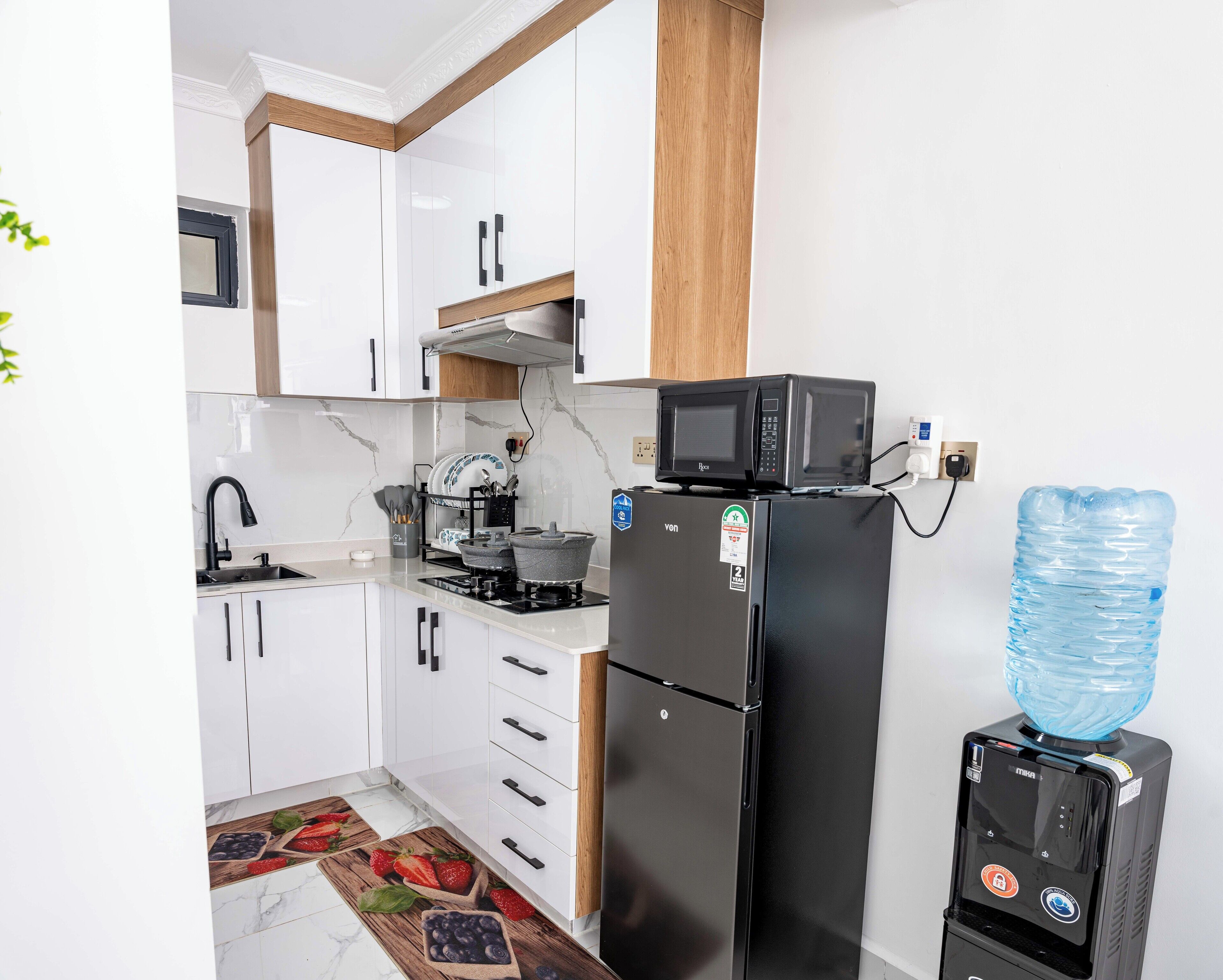 A kitchen with white cabinets, a black refrigerator, a microwave, a water dispenser, and a stove.