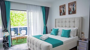 Een slaapkamer met een groot bed, een tafeltje, stoelen en uitzicht op groen.
