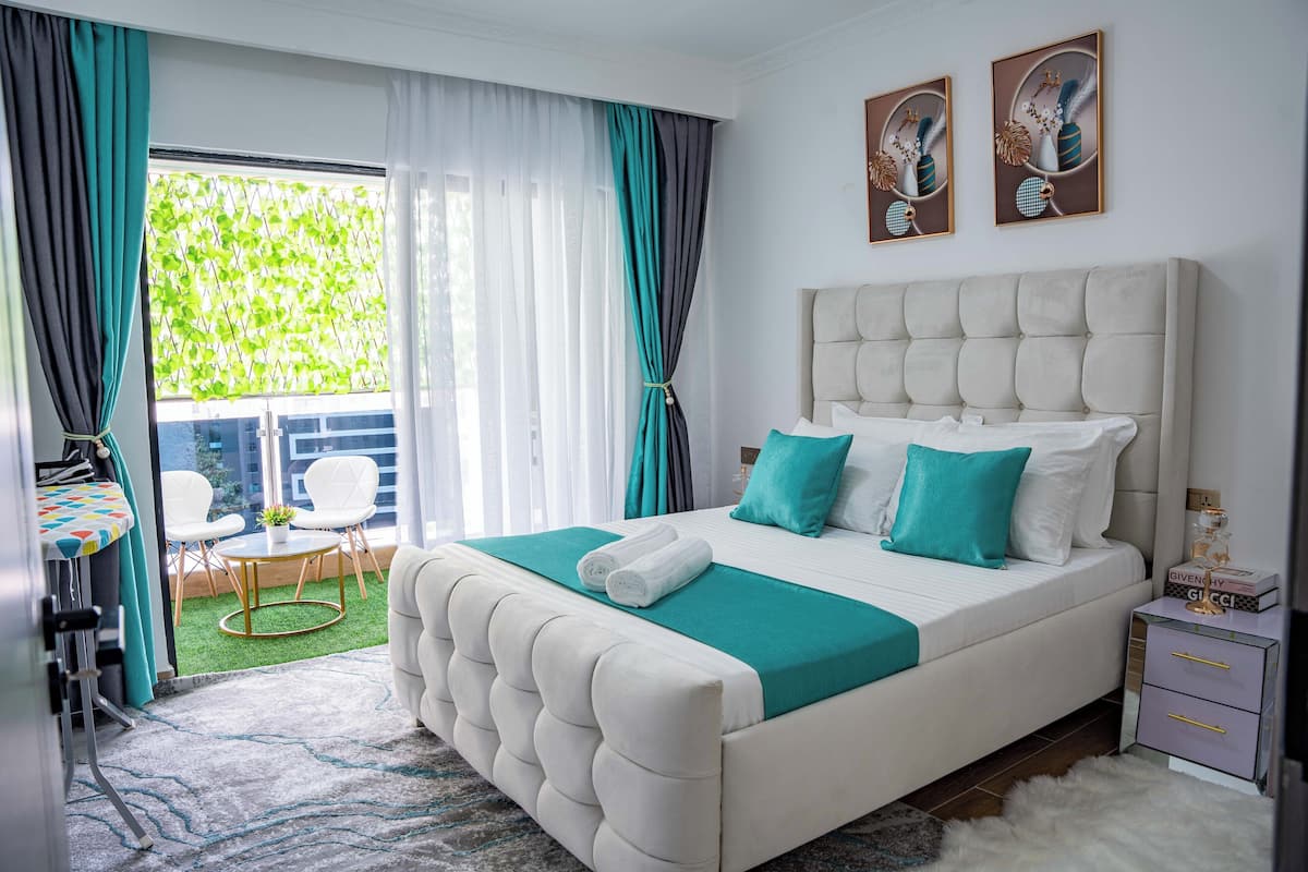 Quarto com uma cama grande, uma mesa pequena, cadeiras e vista para o verde lá fora.