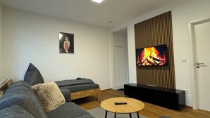 A modern living room with a grey sofa, a small round coffee table, a flat-screen TV mounted on a wooden panel, and a framed picture on the wall. - Stylish apartment in a central location (Dissen am Teutoburger Wald)