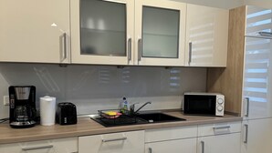 A modern kitchen with white cabinets, a black coffee maker, a microwave, and a sink. - Stylish apartment in a central location (Dissen am Teutoburger Wald)