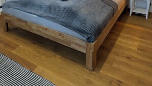 A bedroom with a wooden bed, a radiator, a window with blinds, two bedside tables with lamps, and a framed artwork on the wall. - Stylish apartment in a central location (Dissen am Teutoburger Wald)