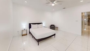 A modern bedroom with a large bed, a ceiling fan, and a nightstand with a lamp. - 2BD-RemoteWork-Extd Stay Discounts-PetsOK-Central (Corpus Christi)