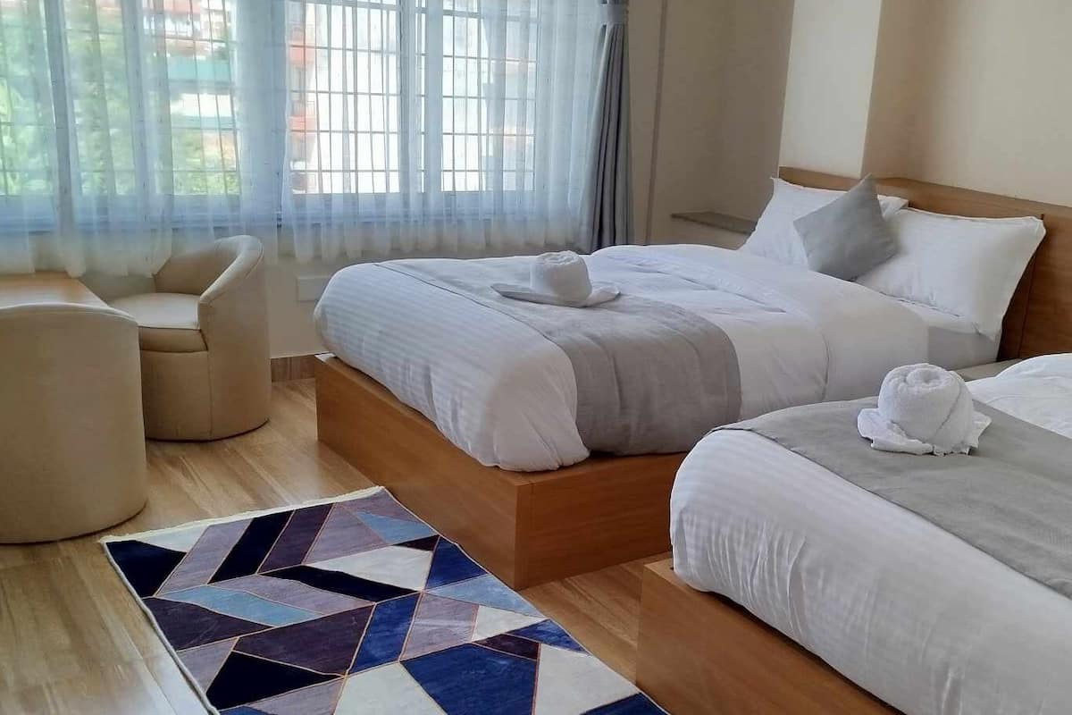 Habitación de hotel con una cama grande, una cama más pequeña, una silla y una alfombra.