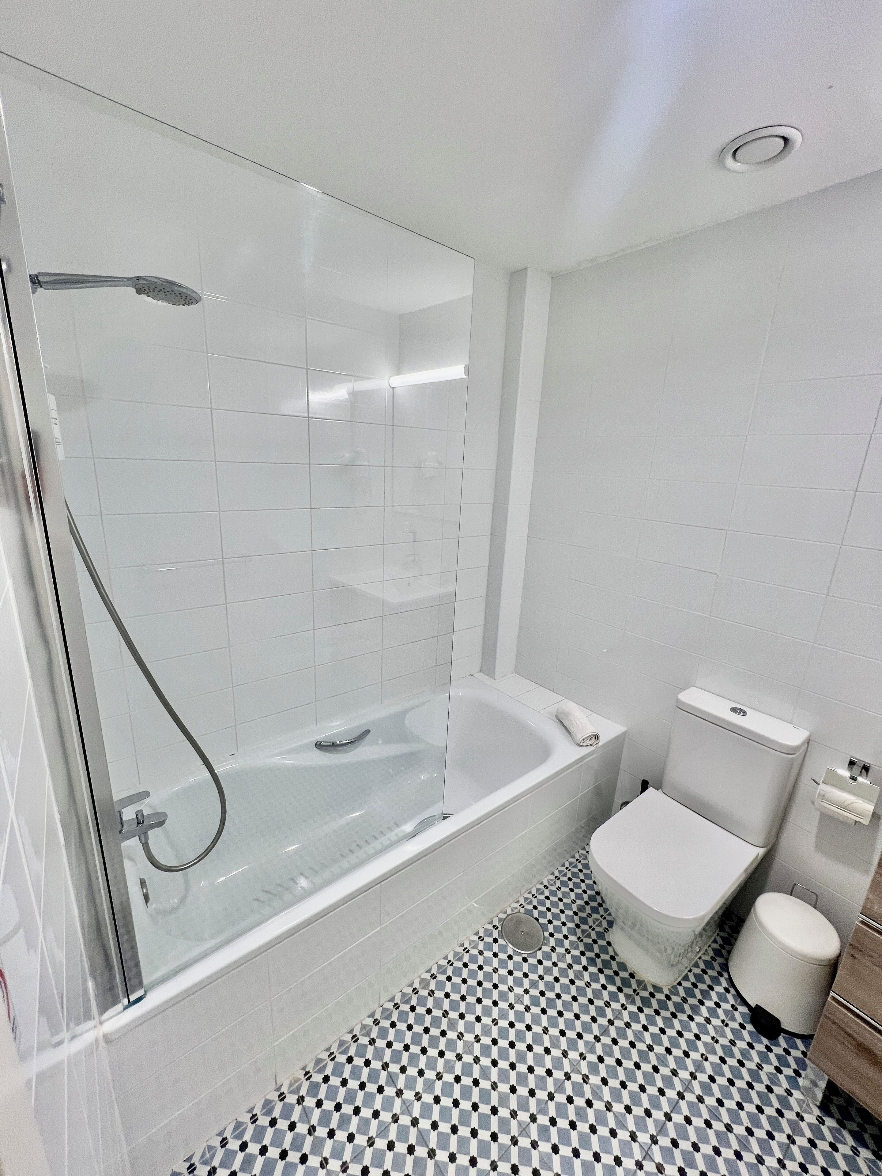 Un baño moderno con ducha envuelta en vidrio, una bañera independiente, un inodoro y un suelo estampado.