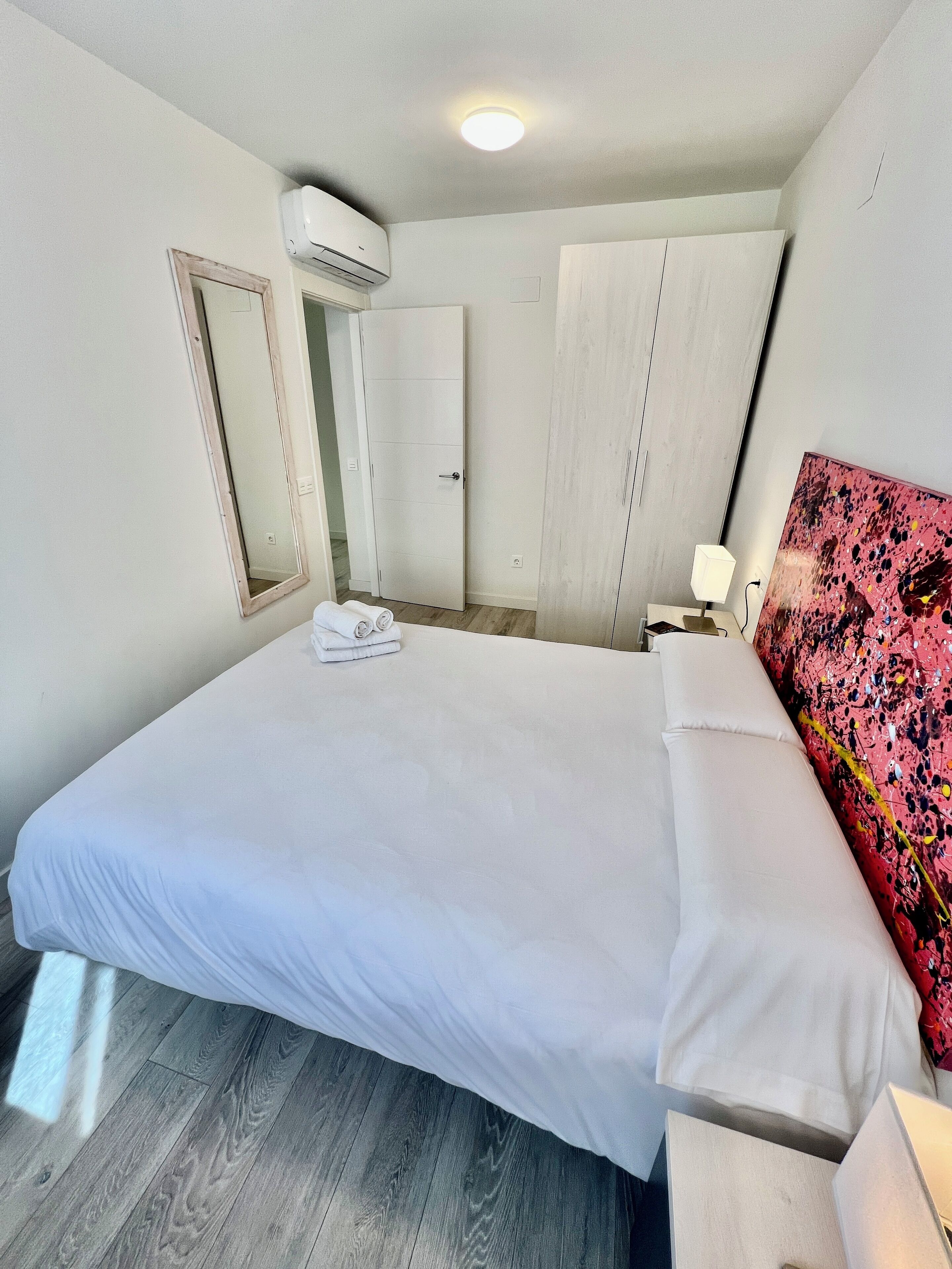 Een slaapkamer met een groot bed, een garderobe, een spiegel en een airconditioning.