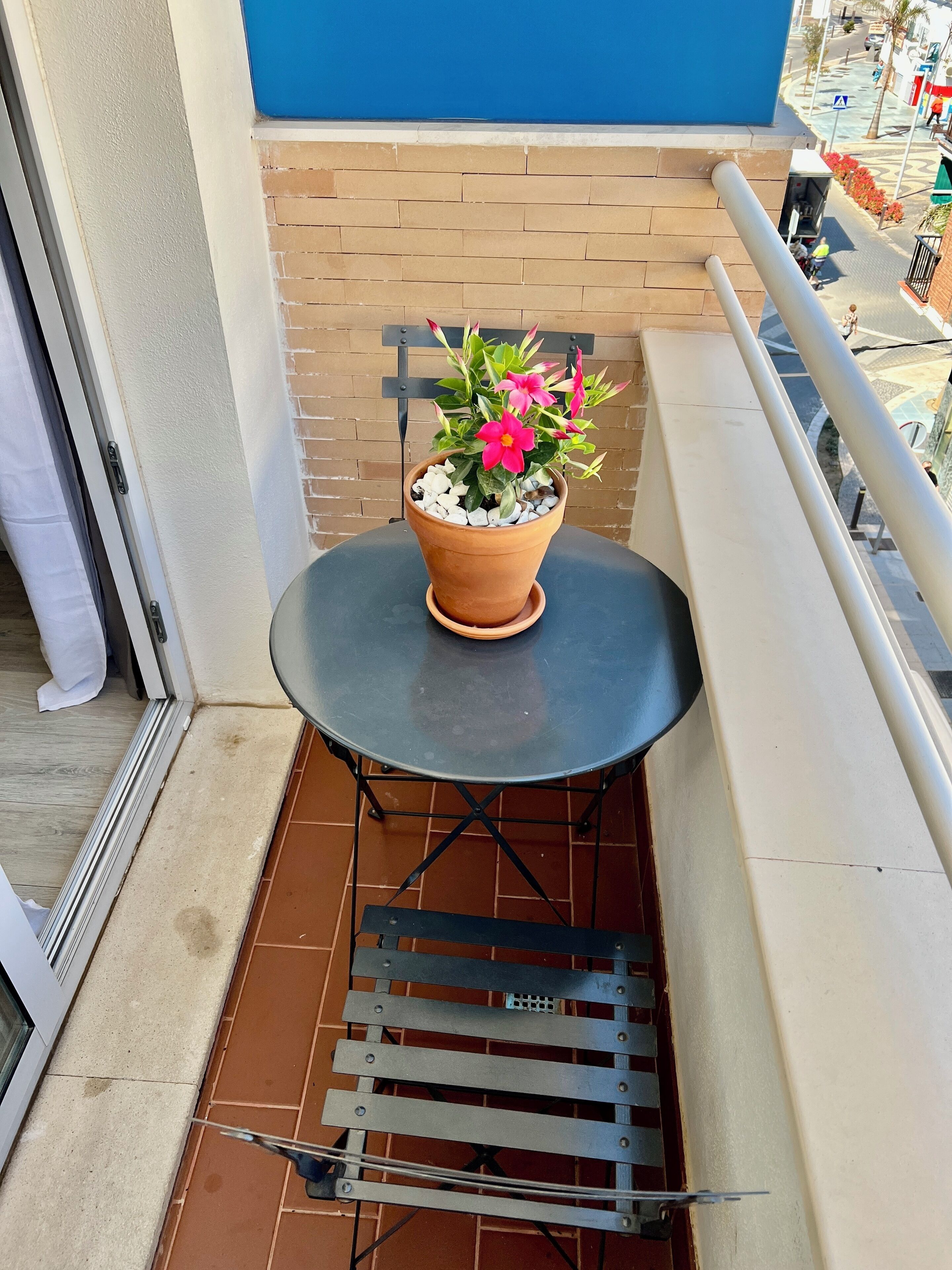A balcony with a potted plant, a small round table, and a metal bench.
